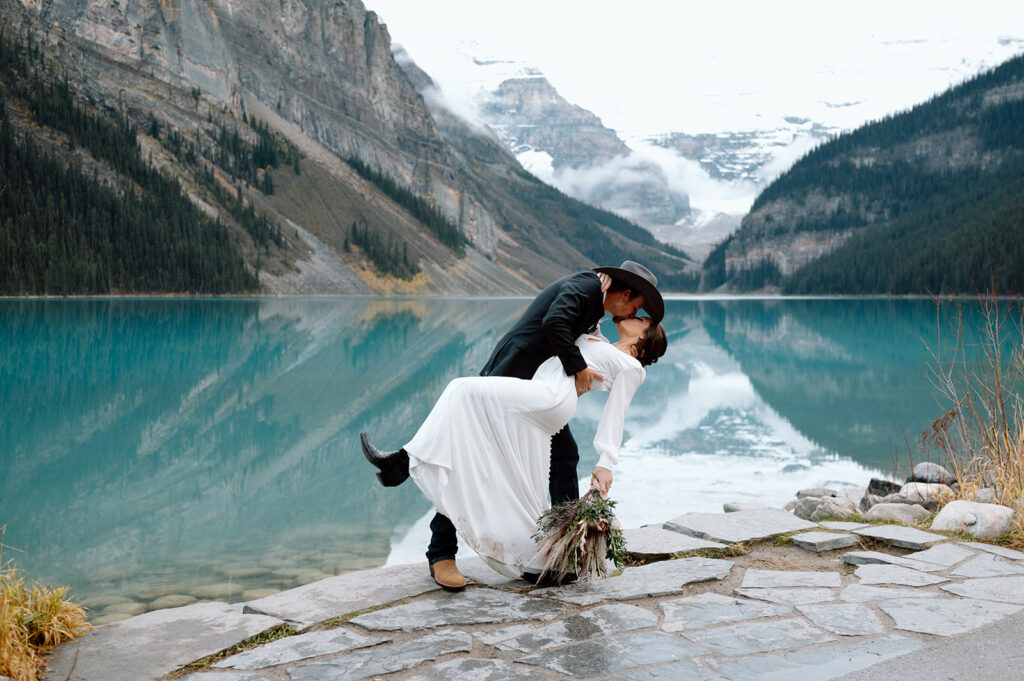 A man dips his bride on the shores of Lake Louise during their intimate Banff elopement.