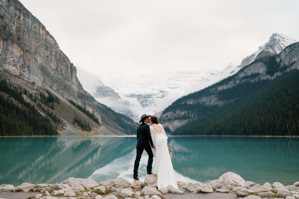 A couple shares a kiss after saying I Do next to Lake Louise. 