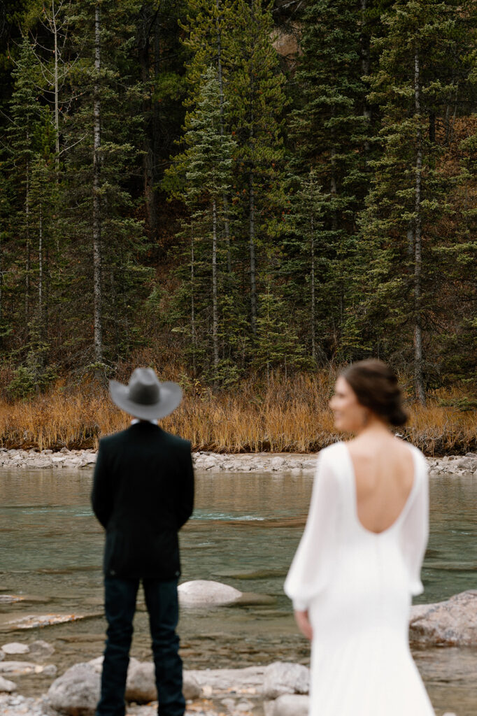 A groom stands with his back towards his bride before their Banff first look. 