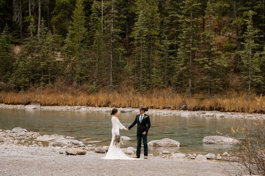 An intimate Banff elopement couple hold hands near a stream near Lake Louise in Alberta. 