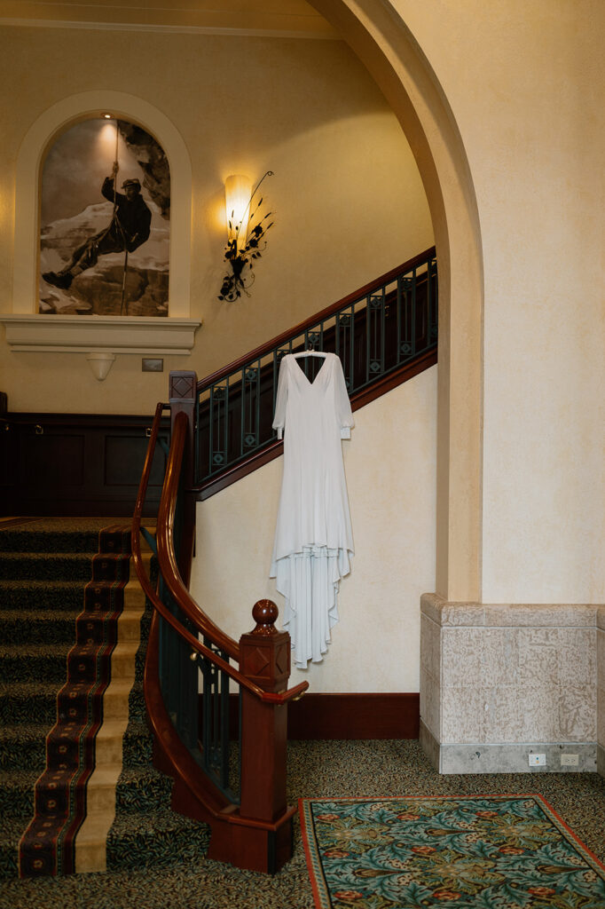 A long white wedding gown is hung from a wooden and carpeted staircase at Fairmont Chateau Lake Louise. 