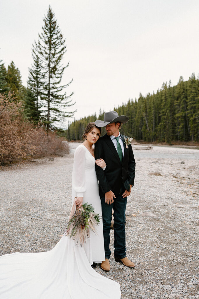 A woman in a long sleeved white bridal gown holds a dried floral bouquet with greenery from Adventure Floral in Calgary, Alberta. 