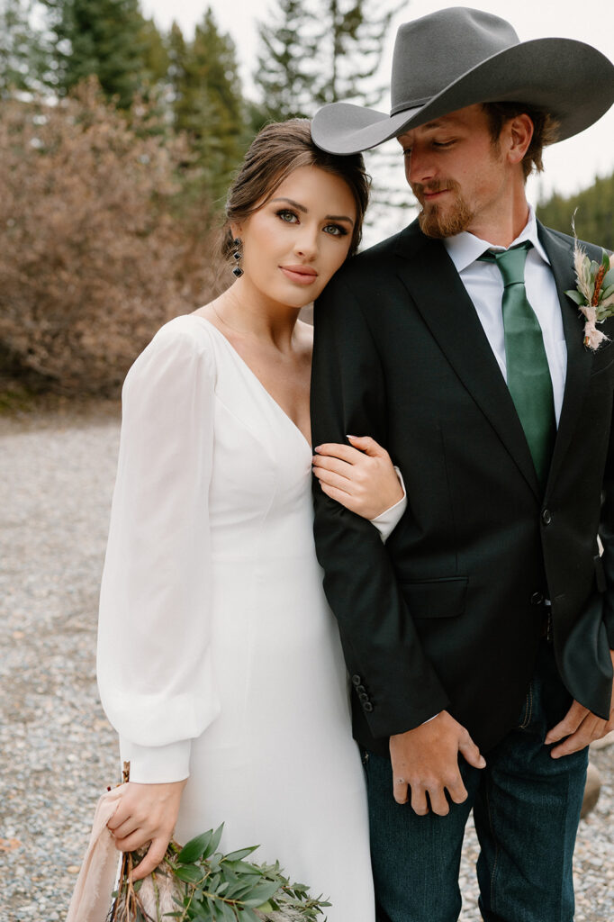 A woman in a white wedding gown embraces her groom in a suit coat and green tie during their intimate Banff elopement. 