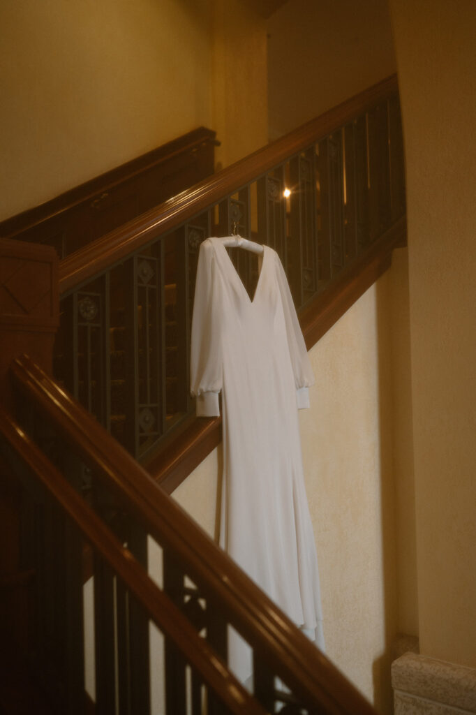 A long white wedding gown hands from a wooden banister along a staircase at the Fairmont Chateau Lake Louise.