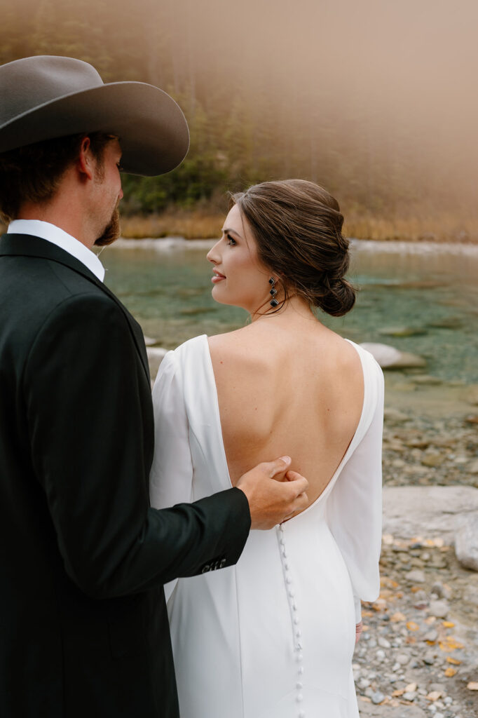 A man strokes his bride's back while they admire a stream in Banff near Lake Louise. 