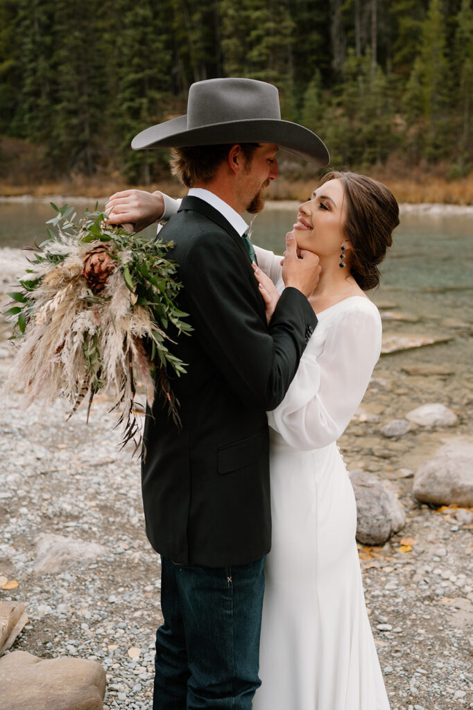 A bride embraces her groom while holding a dried floral bouquet during their Lake Louise elopement. 