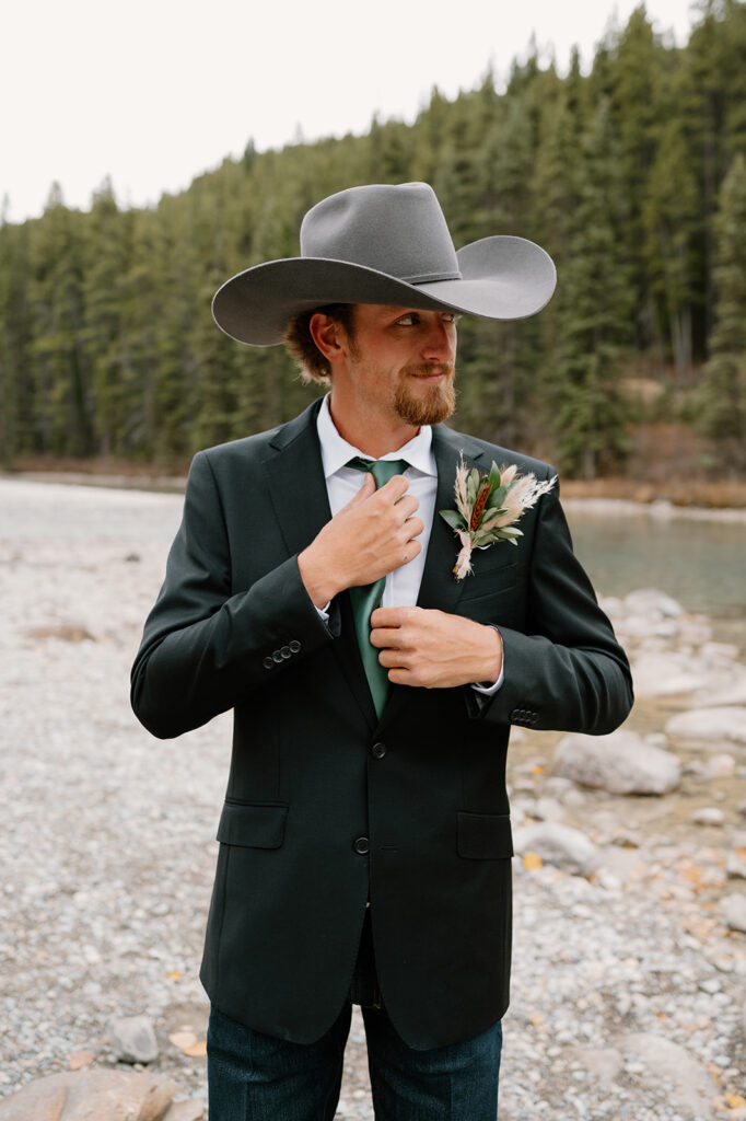 A groom adjusts his green tie while taking wedding portraits during an intimate Banff elopement. 