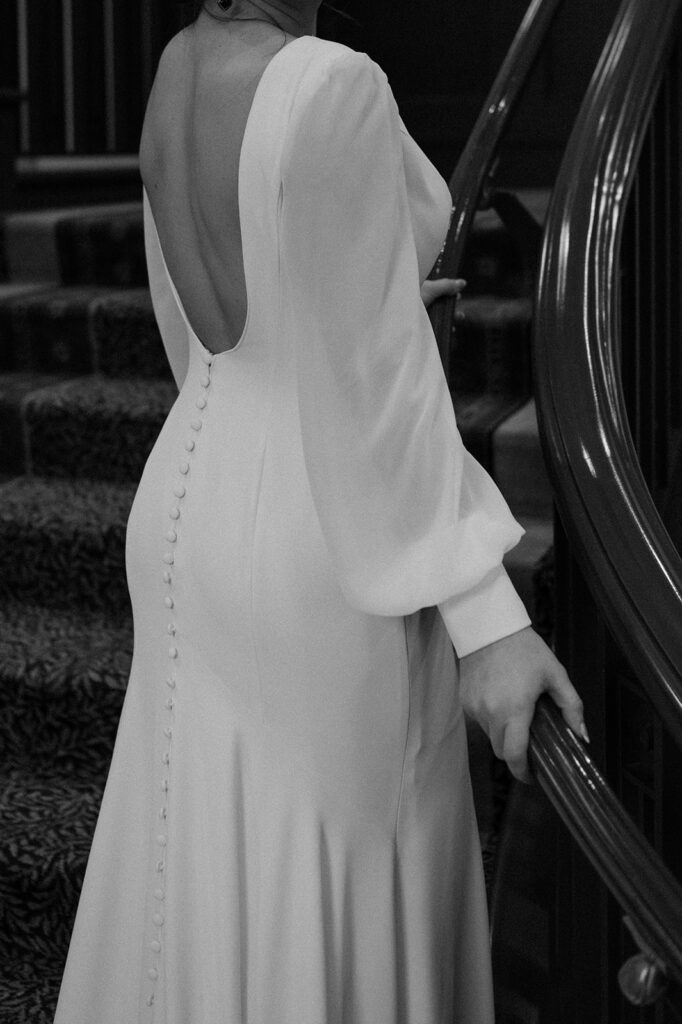 A woman in a long sleeve, floor length white button back wedding dress standing on a staircase at Fairmont Chateau Lake Louise.