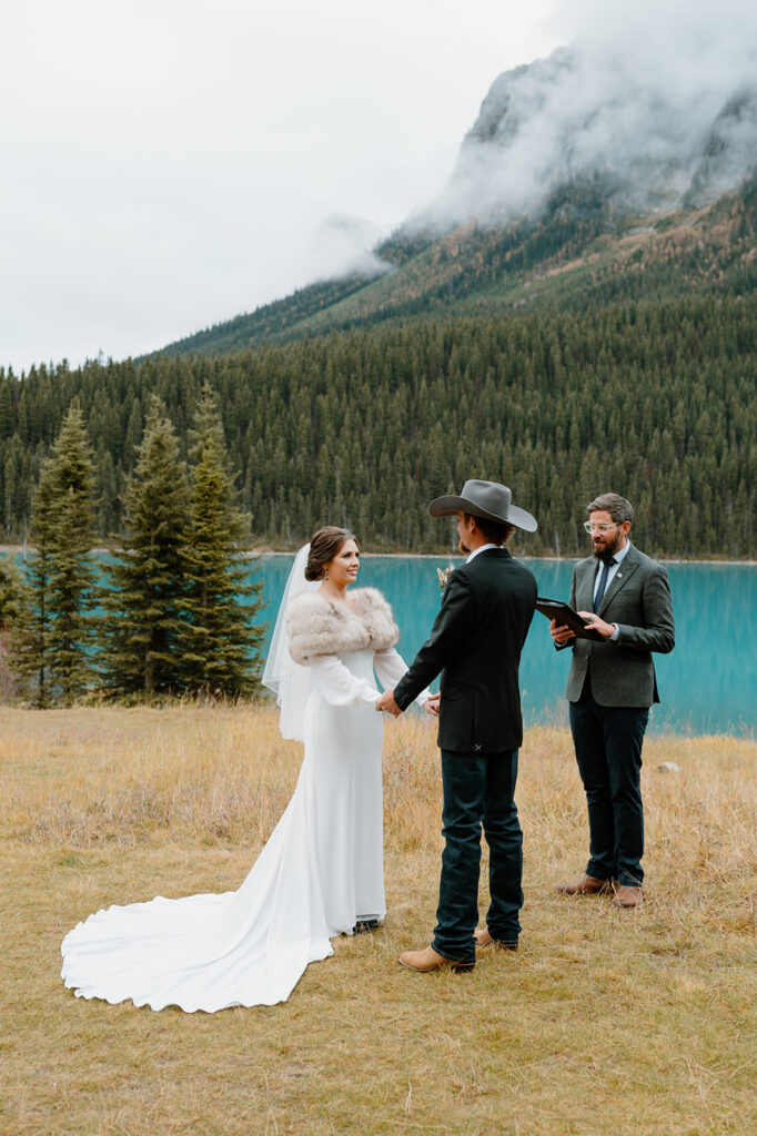 A groom in a cowboy hat and a bride wearing a fur bridal stole say their vows in an intimate Banff elopement ceremony. 