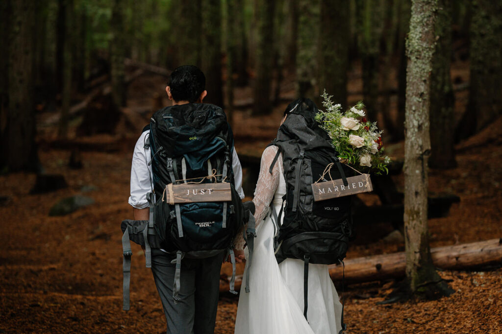 An Oregon adventure elopement couple wears hiking packs with signs that read just married.