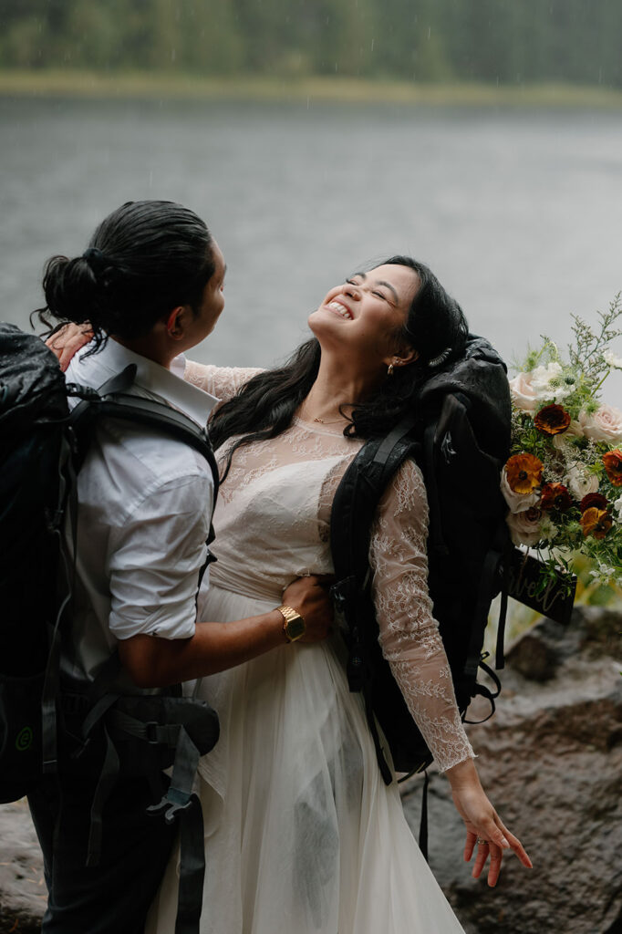 A couple wears wedding attire and hiking packs during their Trillium Lake elopement.