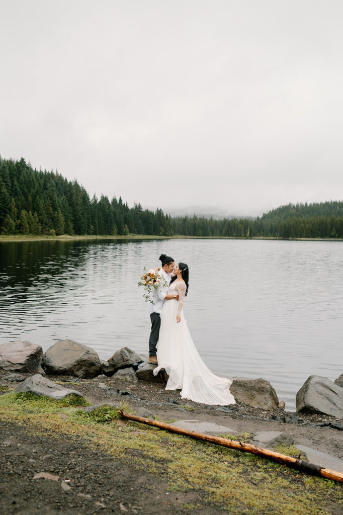 An elopement couple stands on  rocks near Trillium Lake.