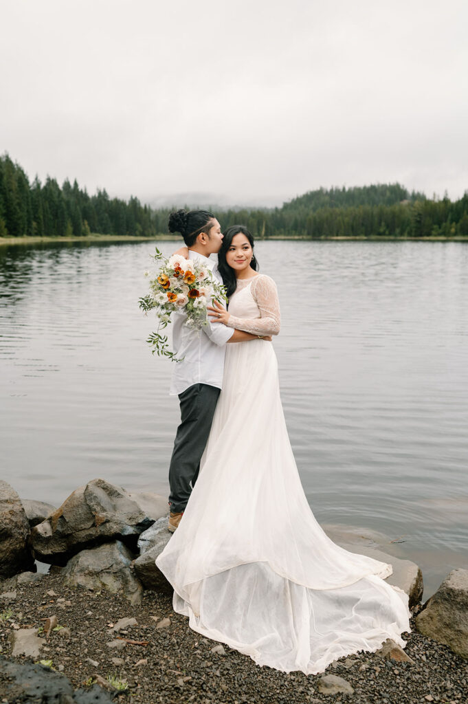 A groom kisses his bride on the shores of Trillium Lake.