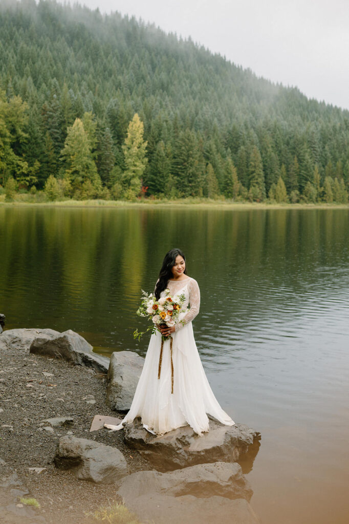 A bride poses on a rock along a lake shore in Oregon.