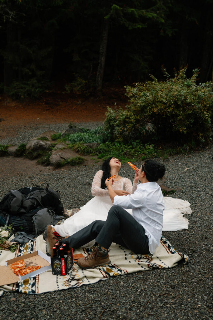 A newlywed couple shares a laugh while eating pizza after their Oregon elopement.