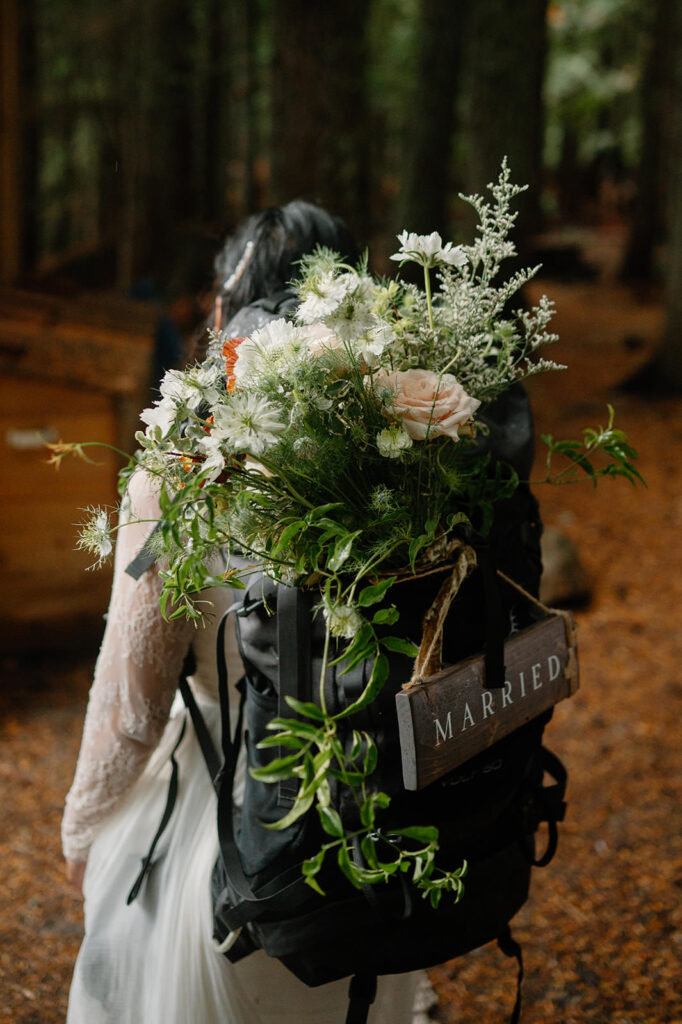 A bride wears a backpack with her bouquet tucked inside. 