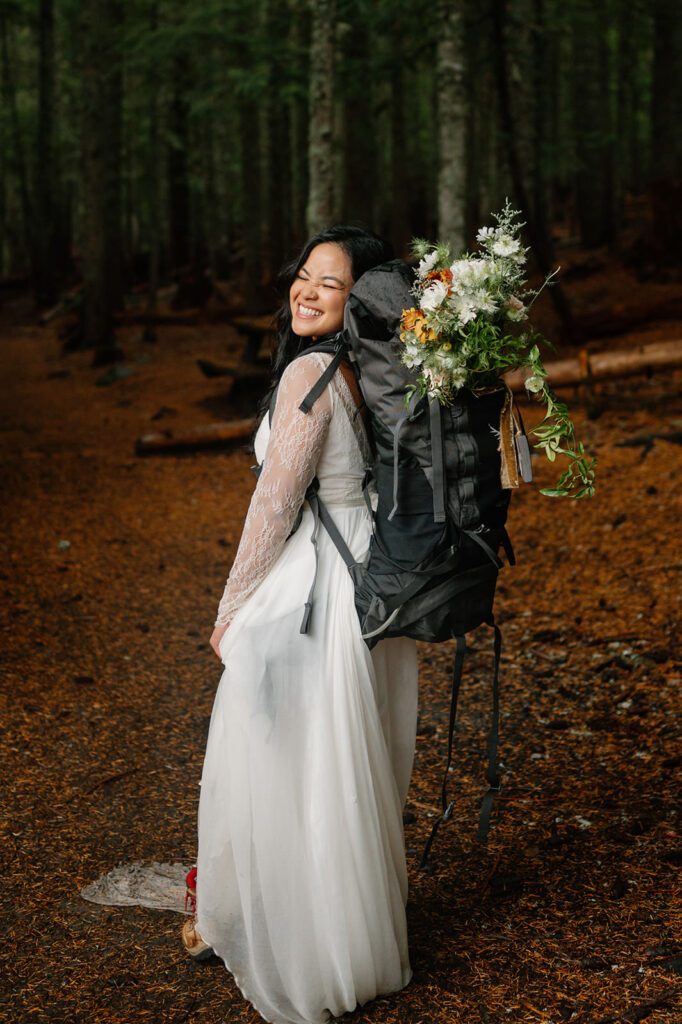 An Oregon elopement bride smiles while wearing a hiking pack.