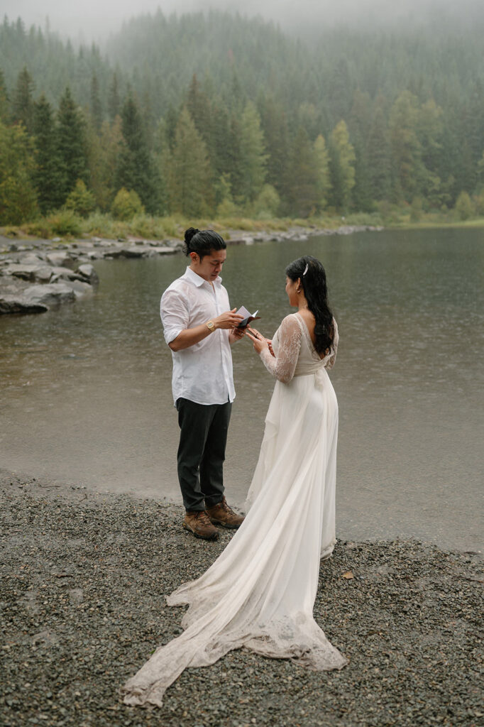 A groom reads is vows from a vow book during an Oregon lake elopement.