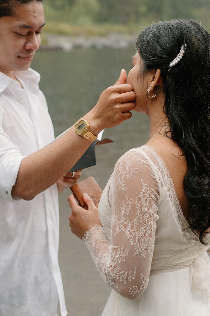 A groom wipes his bride's cheek during a lakeside vow ceremony.
