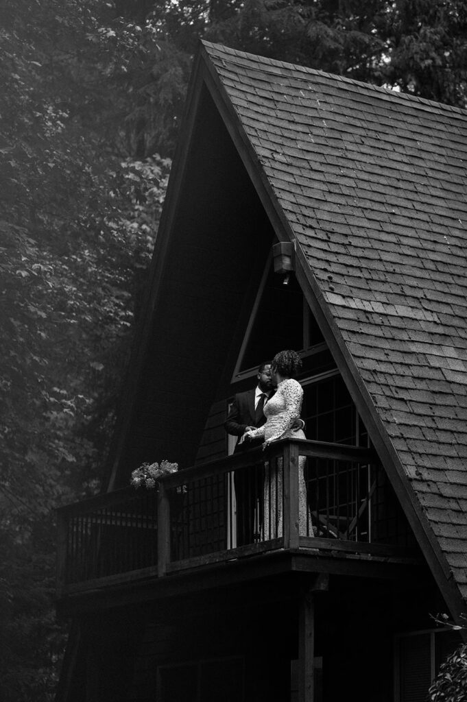 A newlywed couple stands on a balcony of an Oregon Airbnb A-frame.