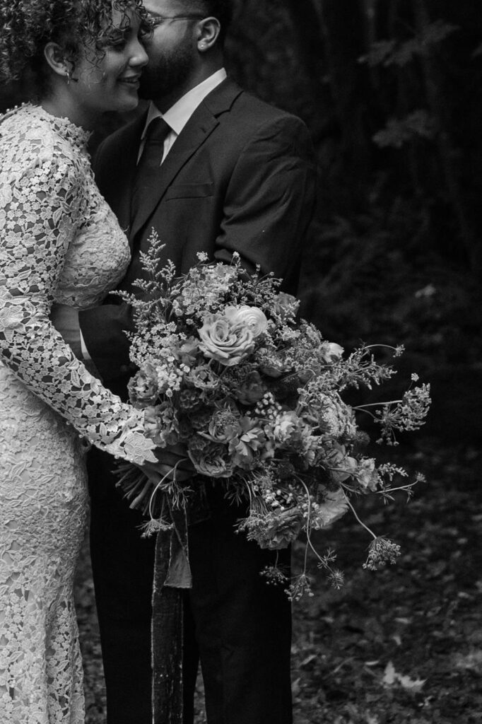 A couple in wedding attire embraces while holding wedding florals.