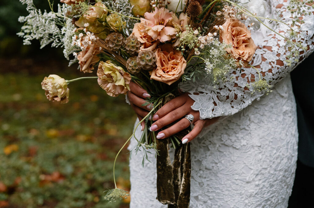 A bride's hands are shown holding a floral bouquet. 