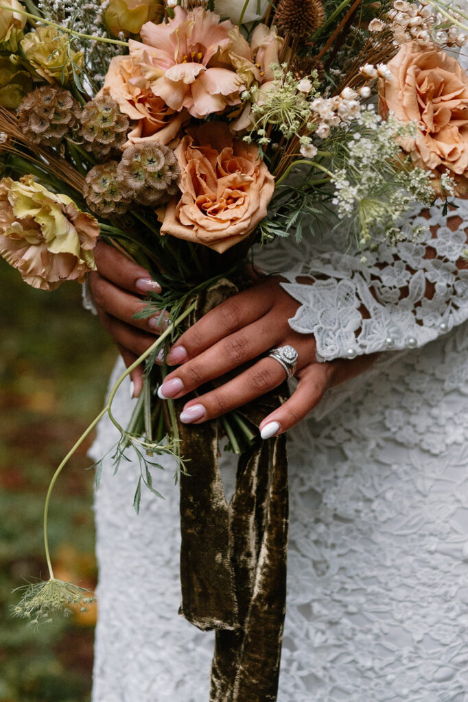 A bride's wedding ring is showcased while holding a bridal bouquet.