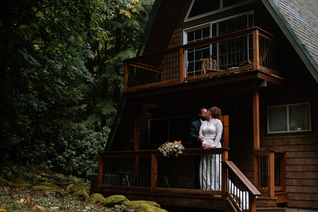 A couple kisses on the porch of an A-Frame Oregon Airbnb.