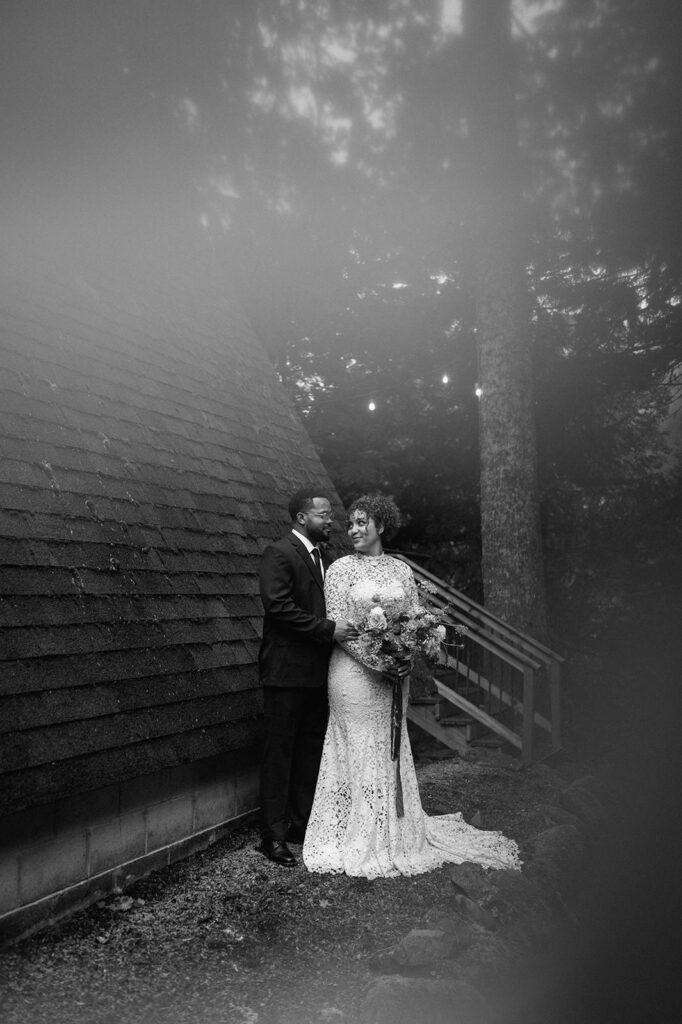 A bride and groom stand near an A-Frame cabin roof. 