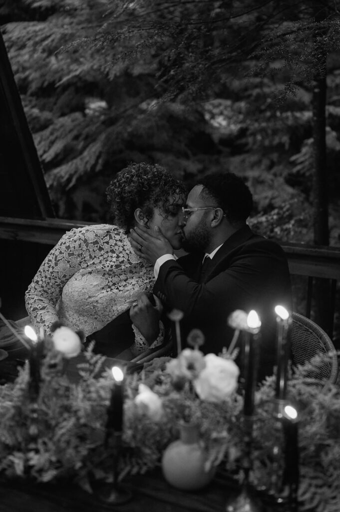 A couple shares a kiss during their intimate wedding dinner reception on a cabin porch.
