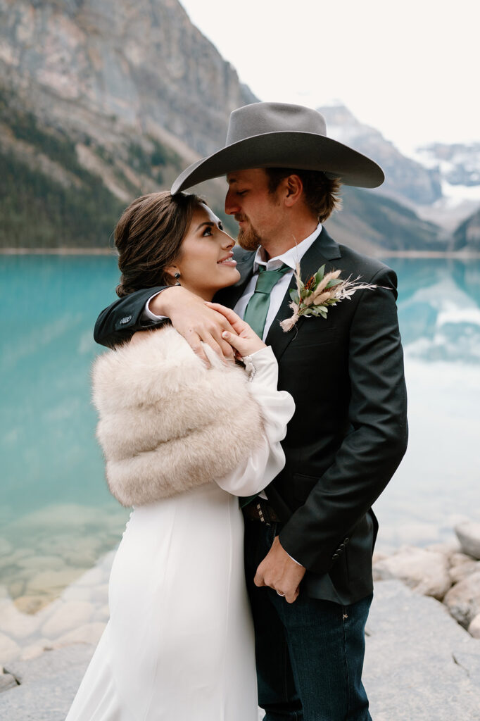 A woman in a fur bridal shawl is held by her husband after their intimate Banff National Park elopement