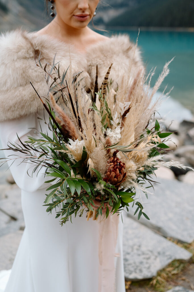 A bride holding a dried floral bouquet from Adventure Floral near Lake Louise.