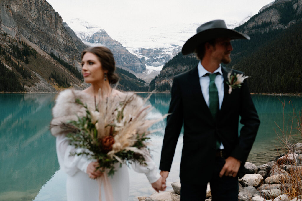 A Banff elopement couple pose for a wedding portrait near Lake Louise with snow-covered mountain peaks in the background. 