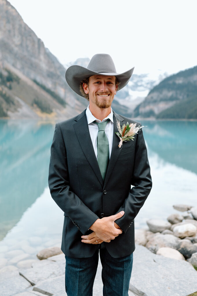 A man is wearing a suit coat, jeans and a cowboy hat near Lake Louise during a Banff elopement. 