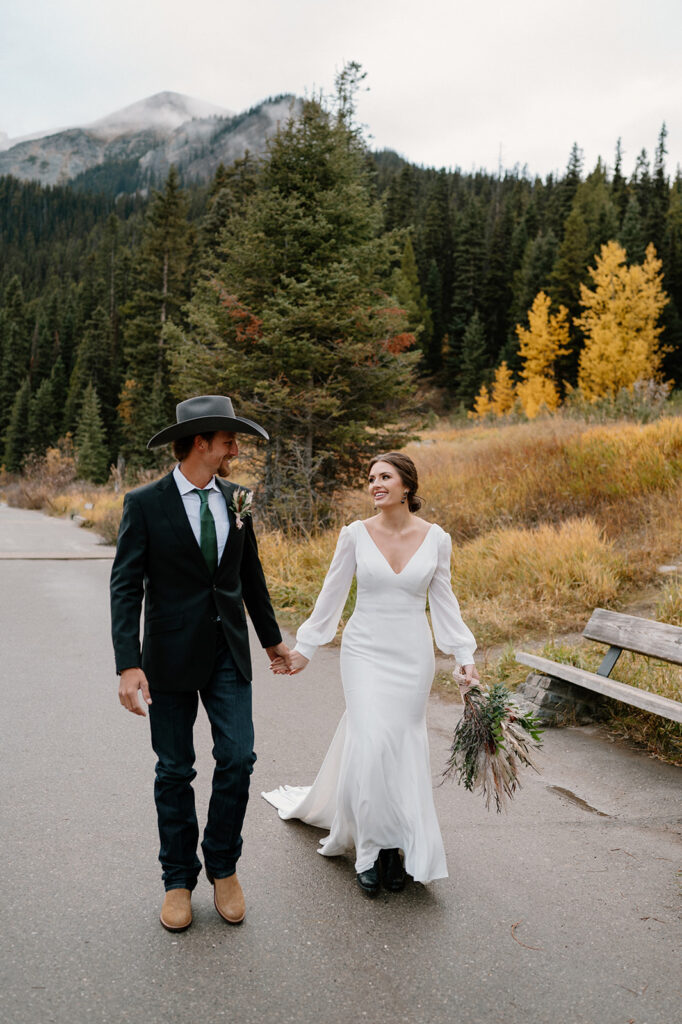 A Banff elopement couple walks along a paved path during Autumn at Lake Louise. 