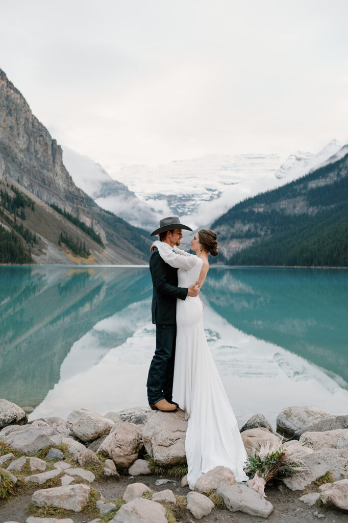 A Banff elopement couple stand on the rocky shores of Lake Louise during their National Park elopement. 