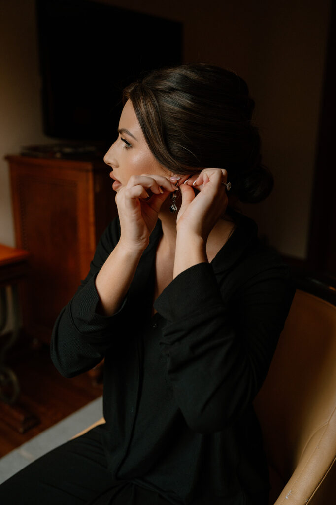 A bride puts on a black drip earring while getting ready at the Fairmont Chateau Lake Louise before her Lake Louise elopement.