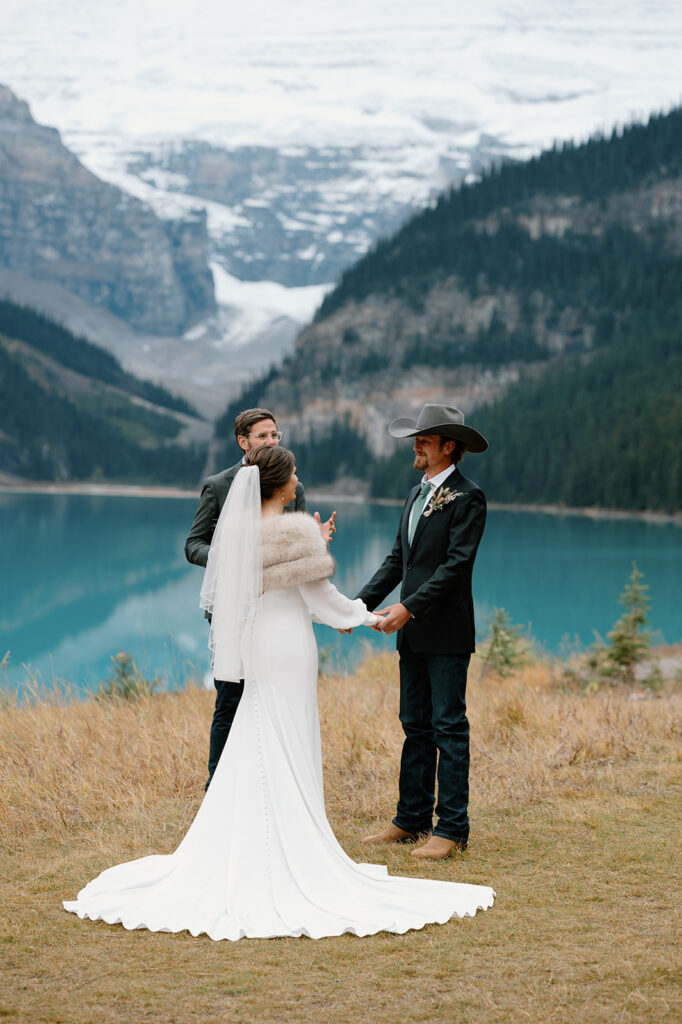 A groom is seen smiling at his bride during an intimate vow ceremony on Lake Louise in Alberta. 