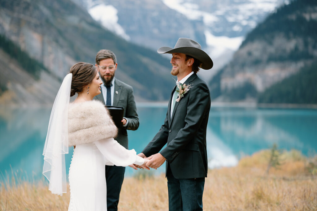 A bride and groom hold hands during an alpine lake vow ceremony in Banff. 