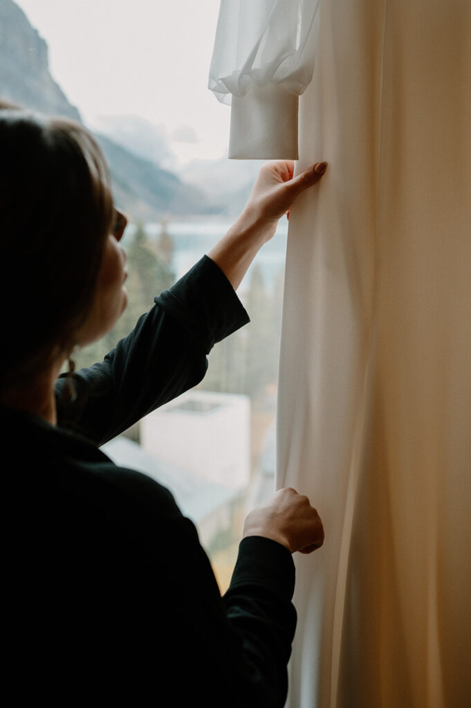 A bride admires her wedding gown that hangs from a window at the Fairmont Chateau Lake Louise. 