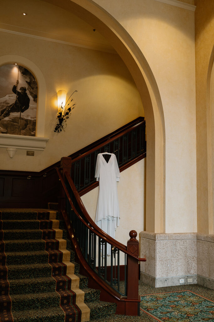 A long white wedding gown hangs from a wooden railing along a staircase at the Fairmont Chateau Lake Louise.