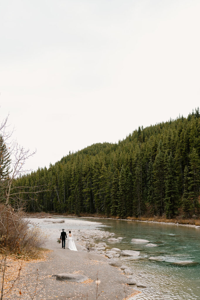 A couple is seen walking while holding hands as they elope in Banff in the Fall near Lake Louise. 