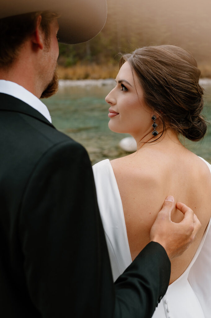 A bride admires her groom as they stand along an alpine stream during their Banff elopement in Alberta. 