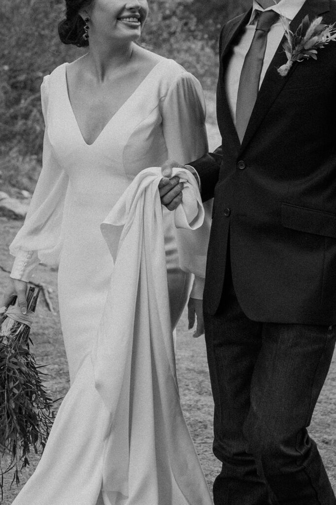 A groom helps carry the train of his bride's long, white wedding gown as they elope in Banff. 