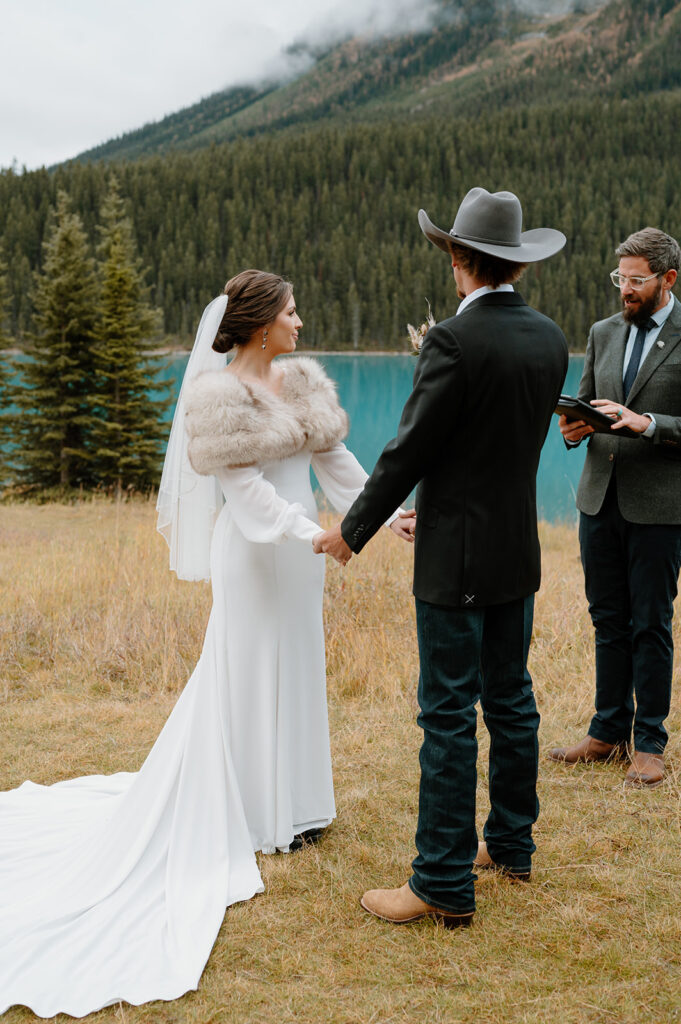 An officiant. bride and groom stand on the shores of Lake Louise as a couple elopes in Banff. 