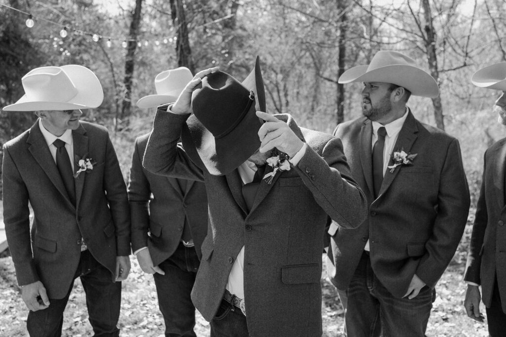 Groomsmen wearing cowboy hats, jeans and suit jackets talk before a microwedding begins. 