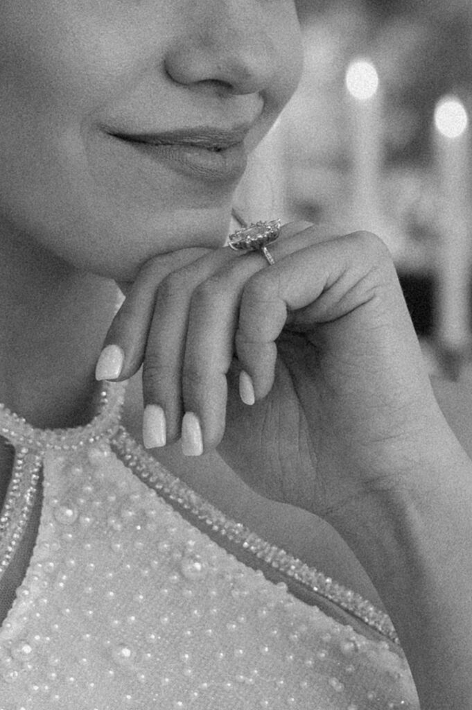 A bride rests her hand on her chin, showcasing a large diamond wedding ring on her finger.