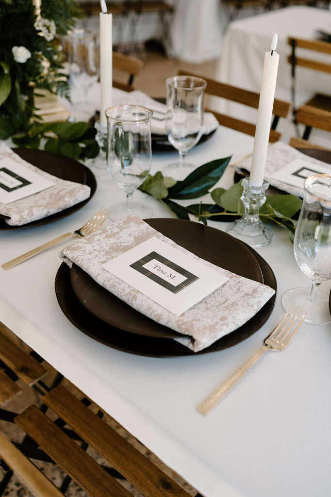 A microwedding place setting featuring a printed napkin, name tag, brown plates, and gold cutlery. 