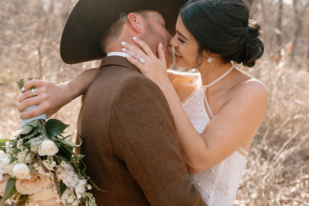 A bride with an updo kisses her groom who is wearing a cowboy hat. 