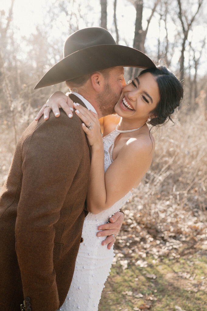 A bride laughs as her groom kisses her on the cheek during their outdoor microwedding. 